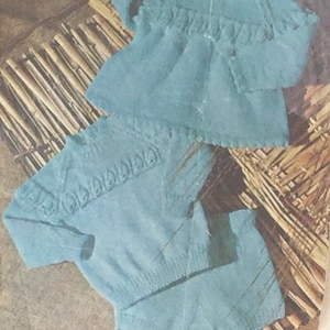 May include: Two light blue knitted sweaters with a delicate lace pattern. The sweaters are laid out on a woven bamboo background.