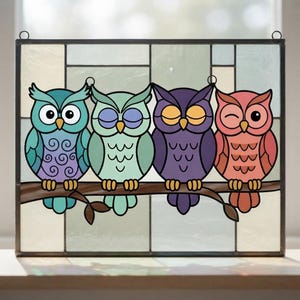Puede incluir: Un panel rectangular de vidriera que muestra cuatro búhos coloridos posados en una rama marrón. Los búhos son de color verde azulado, verde claro, morado y coral, cada uno con expresiones faciales distintas, sobre un fondo de rectángulos de vidrio pálido.
