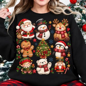 May include: A black sweatshirt featuring a grid of Christmas-themed illustrations including Santa Claus, a snowman, a reindeer, a gingerbread man, a decorated Christmas tree, a penguin, an elf, a polar bear, and a nutcracker.
