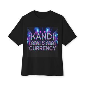 May include: A black short-sleeved t-shirt featuring a central graphic print with the text KANDI IS CURRENCY. The letters and decorative knot patterns are composed of colourful, glowing circular beads against a dark concert stage background.