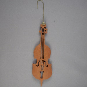 May include: A wooden cutout of a brown cello with a gold hook for hanging. The cello is a Christmas ornament.
