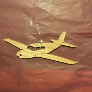 May include: A wooden airplane ornament with a gold hanger. The ornament is a silhouette of a small plane.