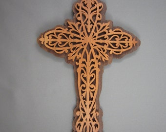 May include: A wooden cross with a decorative, intricate design. The cross is made of dark brown wood with a lighter brown inlay. The design features a series of swirls and curves.