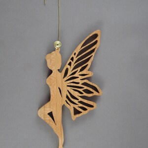 May include: Wooden fairy ornament with intricate cut-out details, featuring a delicate fairy figure with wings and a gold hanger.