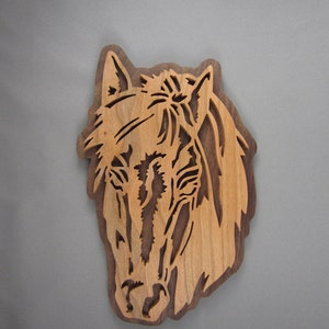 May include: A wooden horse head cutout, carved from a light brown wood with a dark brown grain pattern. The horse's mane and tail are detailed with intricate cuts.