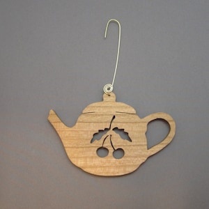 May include: Wooden ornament shaped like a teapot with a cherry and leaves design. The ornament has a gold wire hanger.