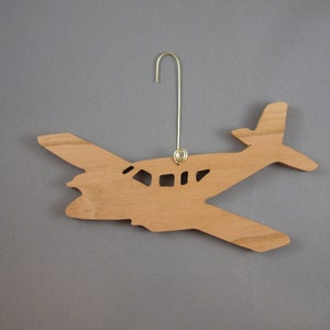 May include: A wooden airplane ornament with a gold-colored wire hanger. The airplane is light brown with cut-out windows and a detailed wing and tail design. The ornament is a decorative item.