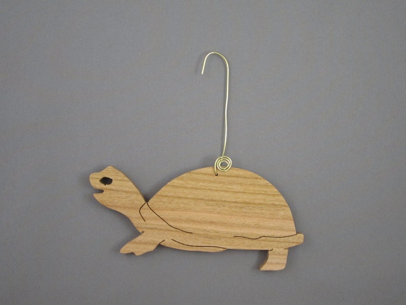 May include: Wooden turtle ornament with a brown finish and a gold wire hanger. The turtle is carved in a simple, stylized design.