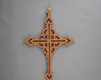 May include: A brown wooden cross ornament with intricate cutouts and a gold hook for hanging.