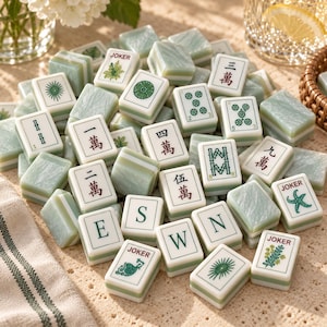 Puede incluir: Una colecci&oacute;n de fichas de Mahjong de color verde claro y blanco con varios s&iacute;mbolos, caracteres chinos y etiquetas Joker. Las fichas tienen una textura marmolada y est&aacute;n esparcidas, mostrando diversas marcas que incluyen E, S, W, N y n&uacute;meros.