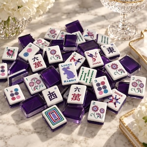 Puede incluir: Una colección de fichas de Mahjong con caras blancas y diseños coloridos de flores, números y caracteres, incluyendo un conejo morado etiquetado como LUCKY RABBIT y fichas de JOKER. Las fichas tienen el reverso y los lados de color morado oscuro translúcido.