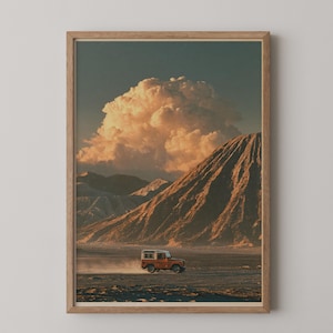 Può includere: Una stampa artistica incorniciata che raffigura un paesaggio con un piccolo veicolo fuoristrada arancione che attraversa un deserto. Sullo sfondo, grandi montagne scoscese si ergono sotto un'enorme formazione nuvolosa illuminata d'oro.