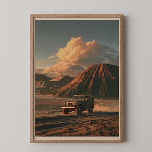 May include: A framed wall art print depicting a dark-colored off-road vehicle driving across a vast, sandy volcanic landscape. In the background, a large, textured mountain rises under a sky filled with golden-hued clouds at sunset.