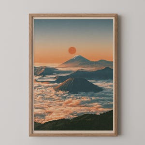 Könnte beinhalten: Ein gerahmter Kunstdruck mit einer Landschaft aus vulkanischen Bergen, die über einer dichten Wolkendecke aufragen. Eine große, orangefarbene Sonne befindet sich in der Mitte eines sanften Himmels über dem schneebedeckten Gipfel des Berges.