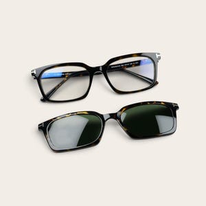 May include: Tortoiseshell-patterned eyeglasses with clear lenses and a matching tortoiseshell-patterned clip-on sunglass attachment with dark green lenses. Both pieces feature a signature T-shaped metal accent on the outer frame corners.