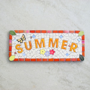 Puede incluir: Un letrero de mosaico con la palabra "SUMMER" en letras naranjas. El letrero está rodeado por un borde rojo y tiene una pequeña mariposa amarilla y flores en el centro.