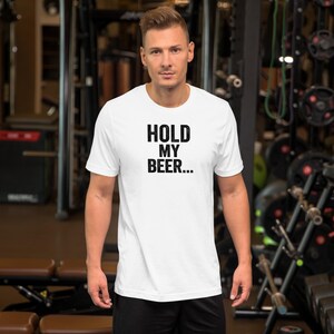 Peut inclure: Un t-shirt blanc à manches courtes avec le texte noir "HOLD MY BEER..." imprimé dans une police sans empattement en gras au centre de la poitrine. Le vêtement présente une encolure ronde classique et un ourlet droit, offrant un design simple.