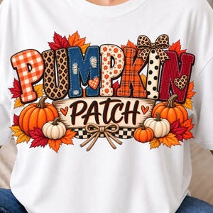May include: A white t-shirt featuring a graphic design with the text PUMPKIN PATCH. The letters are filled with various patterns including plaid, leopard print, and polka dots. The design includes orange pumpkins, autumn leaves, and bows.
