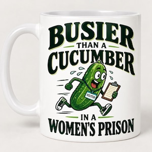 May include: A white ceramic mug featuring a cartoon green cucumber character running while wearing a blue visitor badge and holding a clipboard. The text reads BUSIER THAN A CUCUMBER IN A WOMEN'S PRISON in bold dark green lettering.