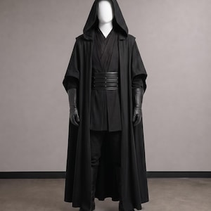 May include: A full-length black hooded cloak worn over a black tunic with a wide, multi-layered black belt. The outfit includes black leather gloves, black trousers, and black boots, all displayed on a white mannequin against a neutral background.