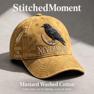 May include: A mustard-colored washed cotton baseball cap featuring an embroidered black raven perched on a crescent moon. The text NEVERMORE is embroidered below the moon, and a feather graphic with the text QUOTH THE RAVEN is on the side.