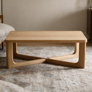 May include: A rectangular coffee table crafted from light-toned wood, featuring a smooth, flat tabletop with rounded corners and a sturdy base composed of four vertical legs connected by a central cross-shaped support structure underneath.