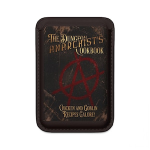 Könnte beinhalten: Ein rechteckiger, dunkelbrauner Kartenhalter mit schwarzem Einband und einem roten Anarchie-Symbol. Der Text lautet The Dungeon Anarchist's Cookbook und Chicken and Goblin Recipes Galore! in goldfarbener, abgenutzter Schrift.