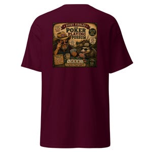 May include: A maroon short-sleeve t-shirt featuring a graphic print of a man and a possum playing poker. The text reads: Dicky Fiddles The Poker Playing Possum, along with various phrases like Best Poker Face In The Animal Kingdom and Possum Poker Strategy.