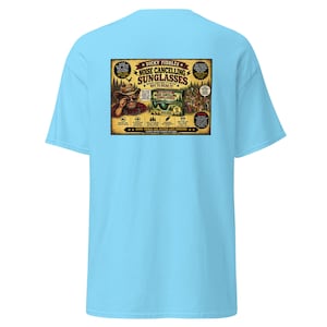 May include: A light blue t-shirt featuring a rectangular graphic on the back. The graphic depicts a cowboy wearing sunglasses with the text "Dicky Fiddles Noise Cancelling Sunglasses" and various humorous product details and illustrations.