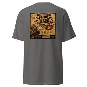 May include: A charcoal gray t-shirt featuring a square graphic on the back. The design depicts a cartoon angler with the text "Dicky Fiddles Xploding Fish Lures" and "Guaranteed to blow up the competition." It includes a warning label and net weight 1.5 oz.