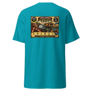 May include: A bright teal short-sleeve t-shirt featuring a rectangular graphic on the back. The graphic depicts a person in a cowboy hat pointing forward, a vehicle with a rooftop tent, and text reading "Dicky Fiddles Penthouse Tent".