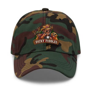 May include: A camouflage baseball cap featuring a graphic of a person in a hat, a deer, and a dog, all wearing sunglasses. The person is pointing forward while holding a mug. Below the graphic, a banner displays the text DICKY FIDDLES in white.