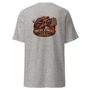 May include: A heather gray t-shirt featuring a graphic on the back. The design shows a man in a hat, a deer, and a dog with the text "DICKY FIDDLES OUTDOOR MARVELS EST. 2026" and "COMMON SENSE... SOLD SEPARATELY" along with other small text elements.