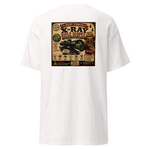 May include: A white t-shirt featuring a large rectangular graphic on the back. The design depicts a rifle scope, a person wearing a hat and sunglasses, and text including "Dicky Fiddles X-Ray Rifle Scopes" and "See What Others Can't!" with various icons.