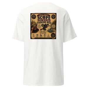 May include: A white t-shirt featuring a large square graphic on the back. The design depicts a fishing rod with a scope, a person in a hat, and a fish jumping from water. Text includes "Dicky Fiddles Scope Powered Fishing Rod" and "See it. Aim it. Scare it. Catch it!"
