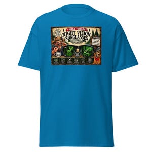 May include: A bright blue short-sleeve t-shirt featuring a graphic print of a person wearing a hat and sunglasses. The text reads "Dicky Fiddles Night Vision Sunglasses" with illustrations of a deer, a person in the woods, and a dog with a red bandana.