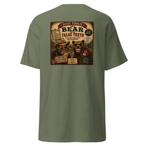 May include: An olive green t-shirt featuring a graphic on the back. The design shows a man in a hat and a bear, both with prominent false teeth. Text includes "Dicky Fiddles The Bear With False Teeth," "Smile Big, Scare Bigger," and "Cavities Optional."