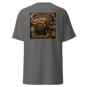 May include: A charcoal gray t-shirt featuring a graphic on the back. The illustration depicts a bearded person in a cowboy hat and overalls pointing forward, with text reading "Dicky Fiddles Countryboy to World Stage" and "From Backwoods to Bright Lights!" along with various small labels.