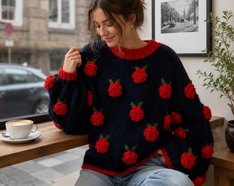 May include: A navy blue long-sleeve knit jumper featuring a crew neckline and ribbed cuffs in a contrasting bright red. The jumper is decorated with multiple three-dimensional red rose appliqués, each accented with small green leaves.