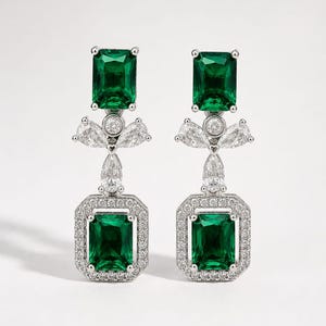 May include: A pair of silver-toned drop earrings featuring a rectangular emerald-green stone at the top and a matching rectangular emerald-green stone at the bottom, surrounded by a halo of small clear stones and accented with three clear pear-shaped stones.