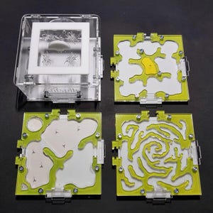 Peut inclure: Un habitat pour fourmis en acrylique transparent comprenant un boîtier principal avec un cadre blanc et trois plaques carrées modulaires. Chaque plaque présente une bordure vert citron et des tunnels internes complexes fixés par des vis.