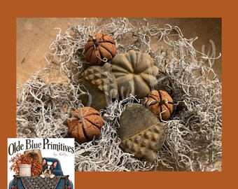 May include: A collection of small, textured, brown decorative pumpkins and acorns nestled within a bed of light gray Spanish moss. The items feature realistic ridges and stems, arranged in a cluster to create a natural, earthy display of autumn-themed decor.