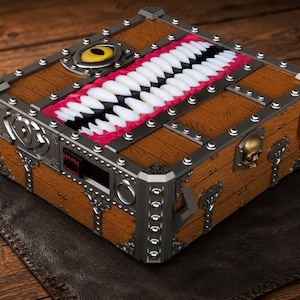 May include: A rectangular wooden chest with a brown wood grain finish, featuring metallic silver corner reinforcements and studs. The lid displays a large yellow eye and a wide mouth filled with rows of white teeth set against a bright red interior.