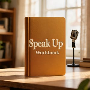 May include: A mustard yellow hardcover workbook with the text Speak Up Workbook embossed in white on the front cover. The book is positioned upright next to a small silver vintage-style microphone on a black stand, featuring a textured finish.