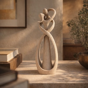 Peut inclure: Une grande sculpture beige texturée représentant deux silhouettes abstraites enlacées. Les personnages sont entrelacés dans une forme fluide et continue avec une finition sablée lisse. La sculpture présente une base large et arrondie qui s'affine vers le haut en une forme unifiée et allongée, créant une sensation de mouvement et de connexion grâce à son design incurvé.
