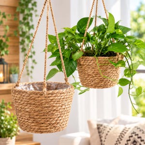 May include: Two hanging planters made of thick, natural-colored woven rope. Each basket features a clear plastic liner inside and is suspended by three matching rope cords. One planter is empty, while the other holds a lush, green trailing plant.