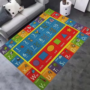 May include: A rectangular educational area rug featuring a colorful grid design. The border displays the alphabet with corresponding illustrations and words. The center section includes numbers one through ten with counting icons and various geometric shapes.
