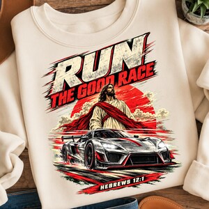 Peut inclure: Un sweat-shirt crème avec une impression graphique portant le texte RUN THE GOOD RACE et HEBREWS 12:1. Le motif représente une silhouette en robe devant un soleil rouge, placée au-dessus d'une voiture de sport argentée aux accents rouges.