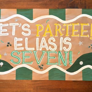 Puede incluir: Una pancarta rectangular con rayas verticales alternas en verde y bronceado con un borde blanco ondulado. El texto dice LET'S PAR-TEE! ELIAS IS SEVEN! con ilustraciones de un carrito de golf amarillo, globos verdes, pelotas y una bandera.