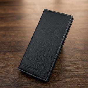 Pode incluir: Uma carteira preta alta e retangular com uma superfície texturizada e granulada. A carteira apresenta costuras brancas em contraste ao longo das bordas e um detalhe de linha horizontal em relevo perto da borda inferior, com um perfil fino.